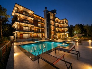 A multi-story hotel with a swimming pool, outdoor seating, and a well-lit facade.