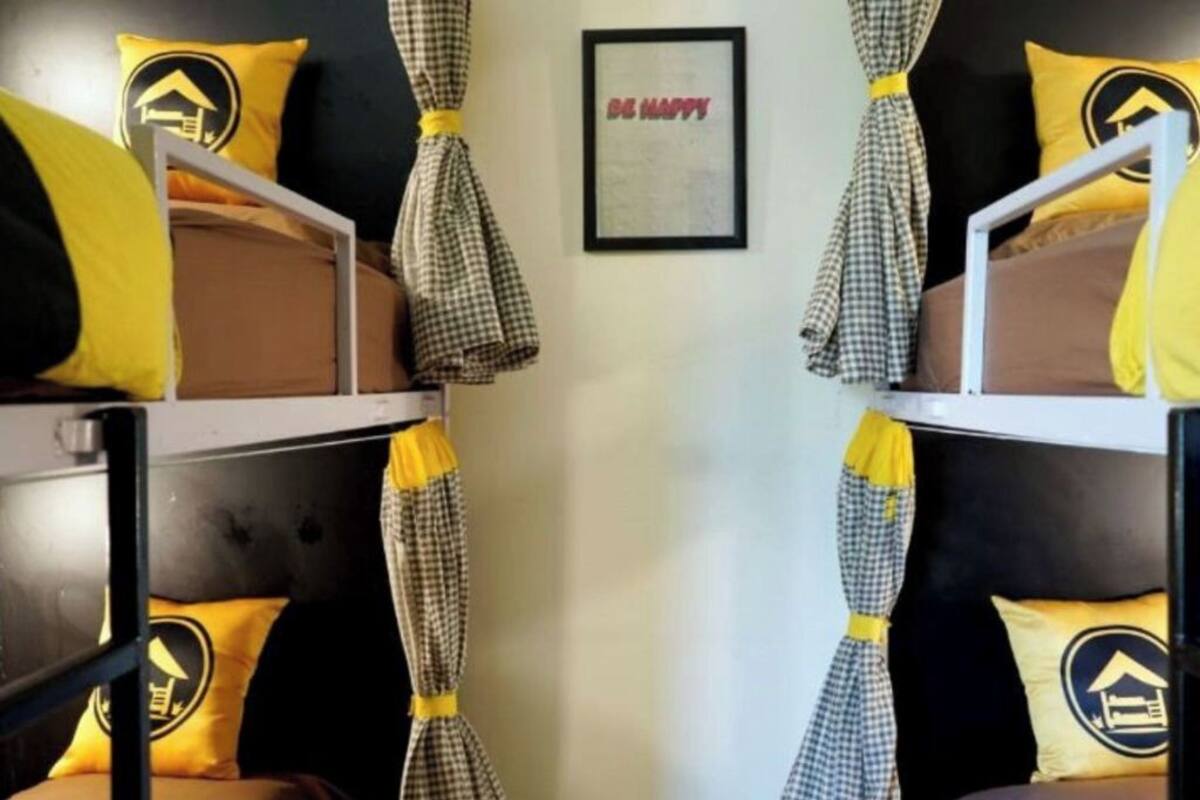 A room with bunk beds, checkered curtains, and yellow pillows with a building logo.
