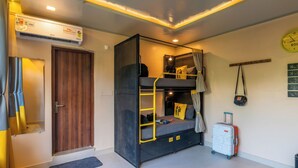 A compact room with a bunk bed, a suitcase, a wall clock, and a ceiling fan. - The Hosteller Bam Bir (Jogindarnagar)