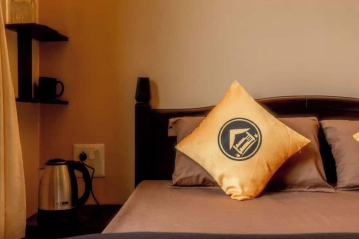 A hotel room with a bed, pillows, a coffee maker, and a shelf with a cup.