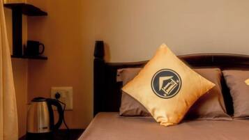 A hotel room with a bed, pillows, a coffee maker, and a shelf with a cup.