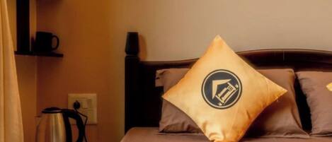 A hotel room with a bed, pillows, a coffee maker, and a shelf with a cup.
