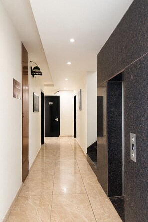 A modern hallway with a marble floor, a black elevator, and a door marked '107'. - Hotel vaikunth (Dharamshala)