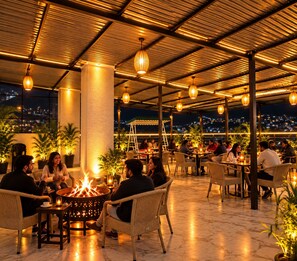 An outdoor dining area with tables and chairs, a fire pit, and potted plants. - Hotel vaikunth (Dharamshala)