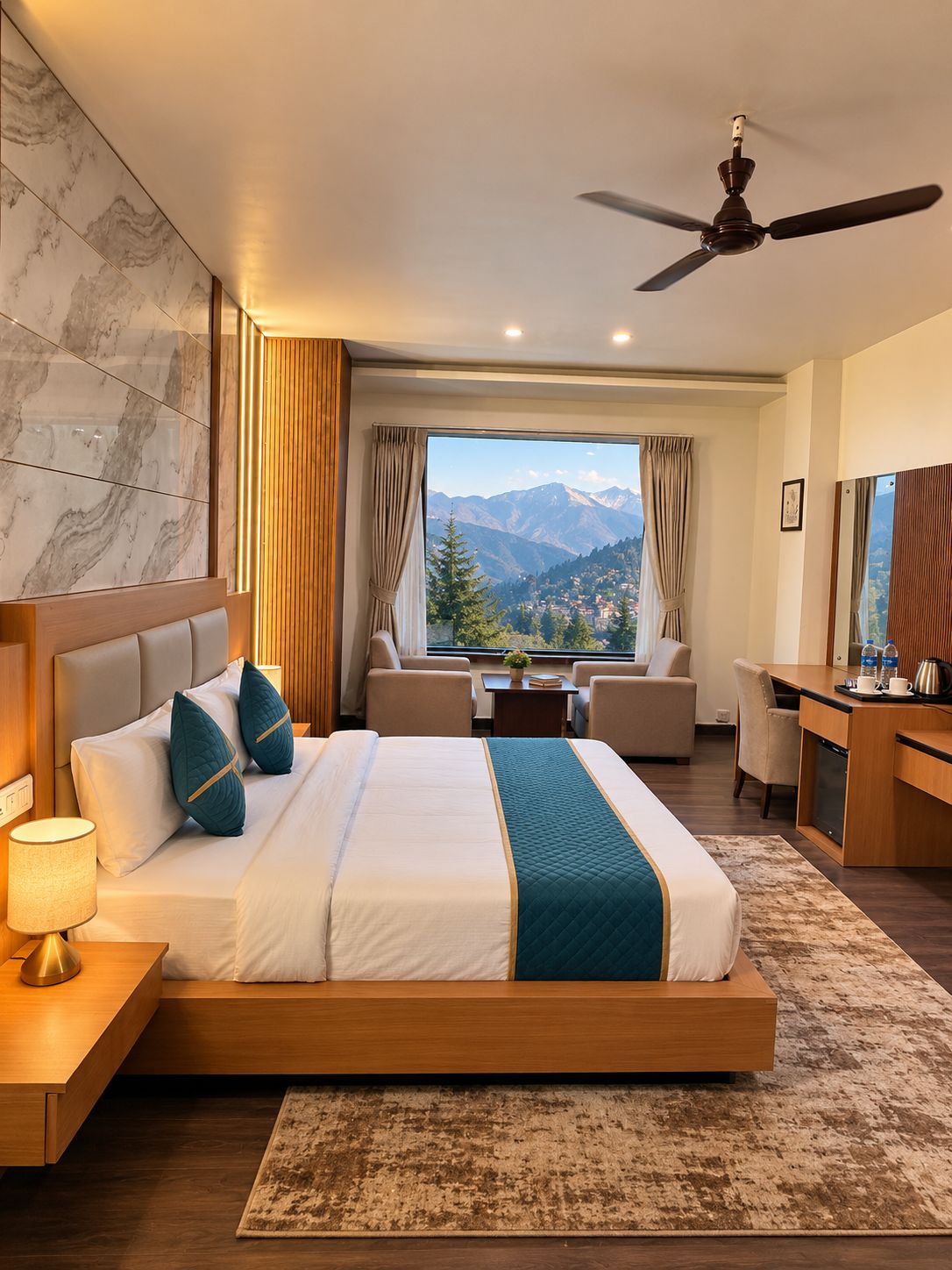 Habitación de hotel con cama, escritorio, silla, vista a montañas y ventilador de techo.