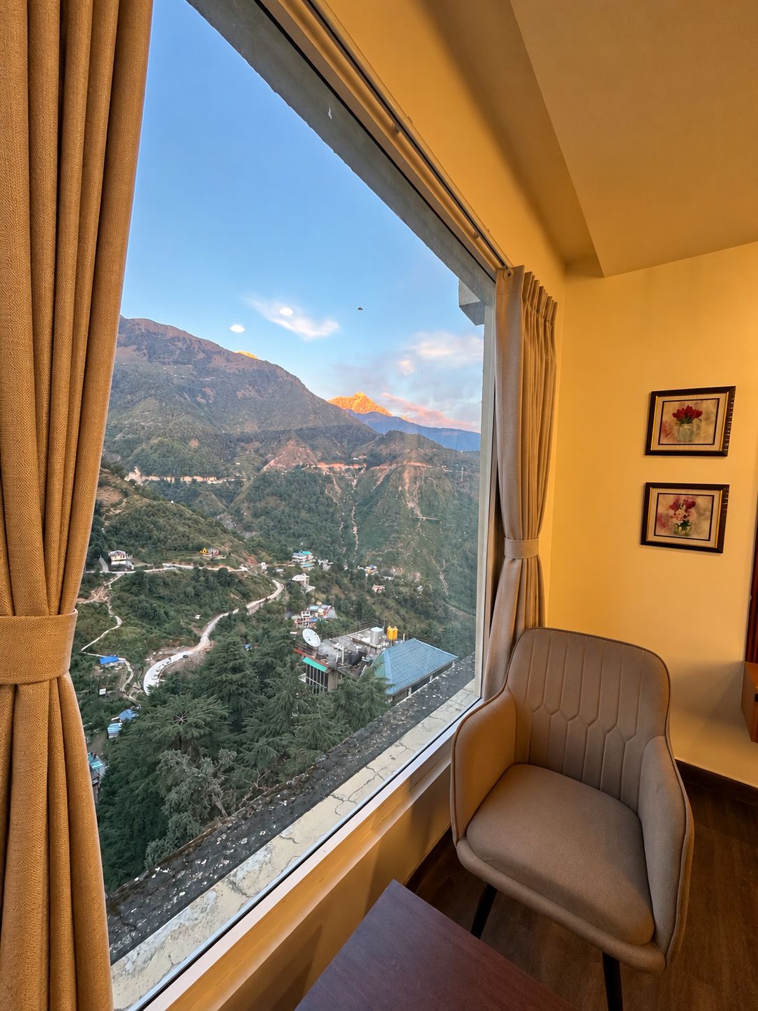 Quarto com vista para uma paisagem montanhosa pela janela, uma cadeira e uma mesa.