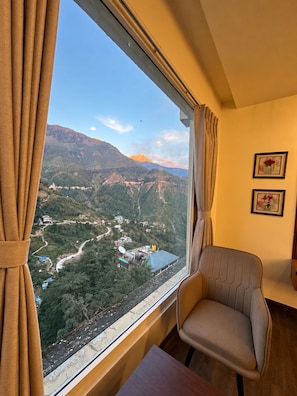 A room with a view of a mountainous landscape through a window, a chair, and a table. - Hotel vaikunth (Dharamshala)