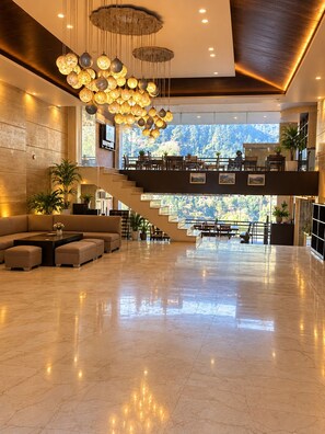 A spacious lobby with a high ceiling, a staircase leading to an upper level, and a seating area with a coffee table. - Hotel vaikunth (Dharamshala)