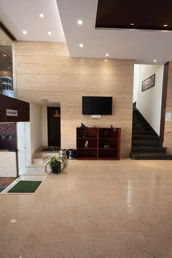 Een hotel lobby met een flatscreen televisie aan de muur, een trap aan de rechterkant en een receptiebalie met een bord waarop een restaurant wordt aangegeven.