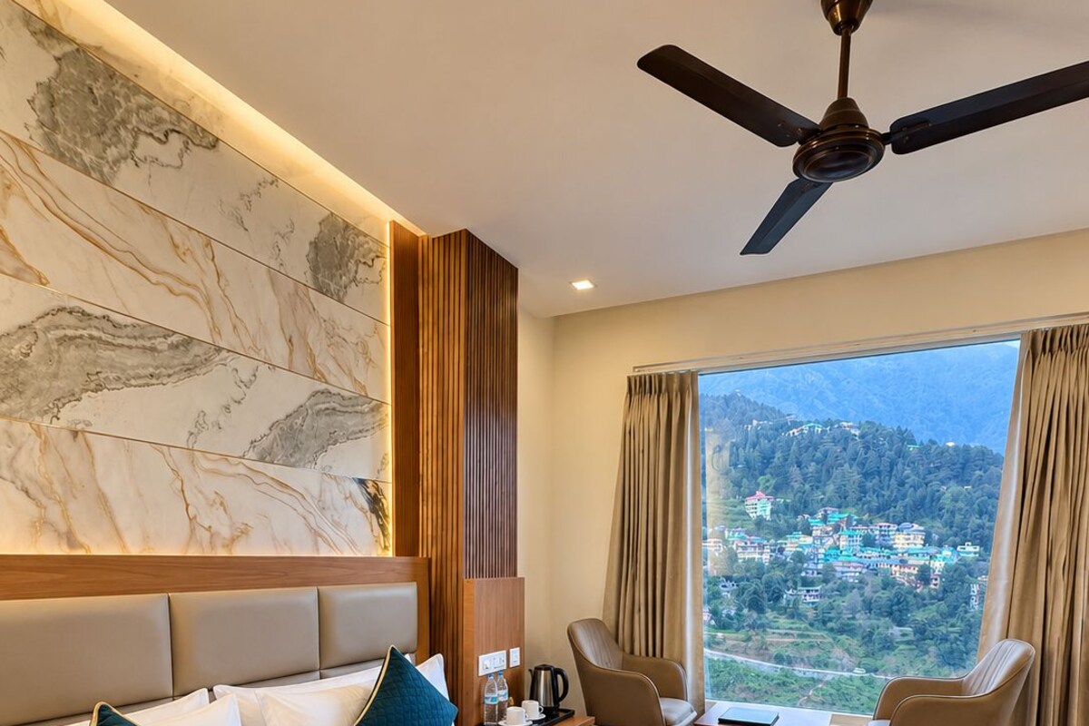A hotel room with a large bed, a ceiling fan, a view of a mountainous landscape, and a seating area with a table and chairs.
