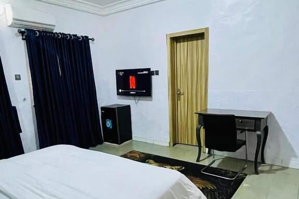Un dormitorio con una cama, un escritorio, un televisor y un equipo de aire acondicionado.