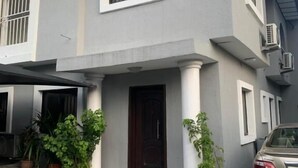 A two-story house with a grey facade, a front porch with columns, and a car parked in the driveway. - Weena Hotel & Resort (Lekki)
