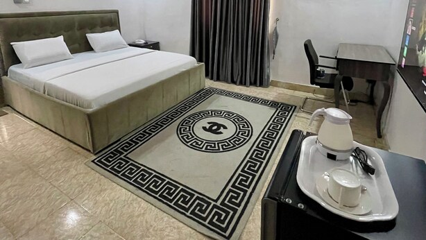 A hotel room with a bed, a desk, a chair, an air conditioning unit, and a coffee maker on a tray. - Weena Hotel & Resort (Lekki)