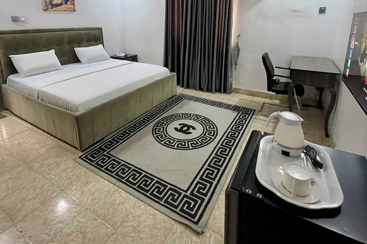 Habitación de hotel con cama, escritorio, silla, equipo de aire acondicionado y cafetera sobre una bandeja.