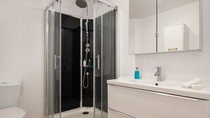 A modern bathroom with a glass-enclosed shower, a white sink, and a mirror above the vanity. - Les Oliviers - 1st Floor Studios by RentalsPro (Vourvourou)