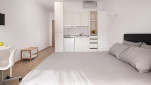 A modern bedroom with a large bed, a desk, and a kitchenette. - Les Oliviers - 1st Floor Studios by RentalsPro (Vourvourou)