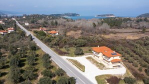 An aerial view of a coastal area with houses, a road, and a beach. - Les Oliviers - 1st Floor Studios by RentalsPro (Vourvourou)