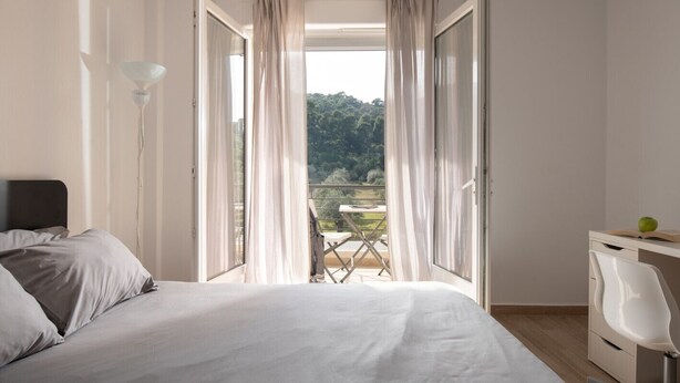 A bedroom with a bed, a desk, and a view of a balcony with a table and chairs. - Les Oliviers - 1st Floor Studios by RentalsPro (Vourvourou)