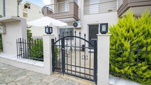 Un edificio residencial con entrada protegida por un portón, un balcón y un seto bien cuidado.