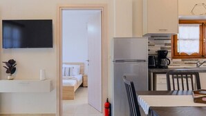 Een moderne keuken met een koelkast, koffiezetapparaat en houten kastjes. Een bed met een gestreept kussen is zichtbaar door een geopende deur.
