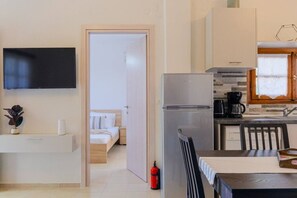 Eine moderne Küche mit Kühlschrank, Kaffeemaschine und Holzschränken. Durch eine offene Tür ist ein Bett mit gestreiftem Kopfkissen zu sehen.