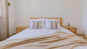Een tweepersoonsbed met gestreepte kussens, een houten hoofdbord, een nachtkastje met een plant en een beige deken.