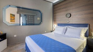 Una habitación de hotel con una cama grande, un espejo, un reloj y una mesita de noche con lámpara.