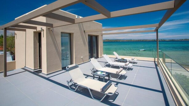 A rooftop terrace with sun loungers, a glass balustrade, and a view of the sea. - Tiamo Secrets - Beach Front by RentalsPro (Vourvourou)