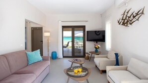 A modern living room with a sofa, coffee table, and TV. - Tiamo Secrets - Beach Front by RentalsPro (Vourvourou)