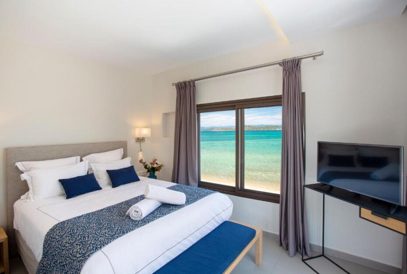 Une chambre d’hôtel avec un lit, une télévision, une fenêtre avec des rideaux et une vue sur la mer.