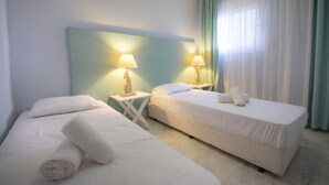Una habitación de hotel con dos camas, una mesita de noche con lámpara y una ventana con cortinas.
