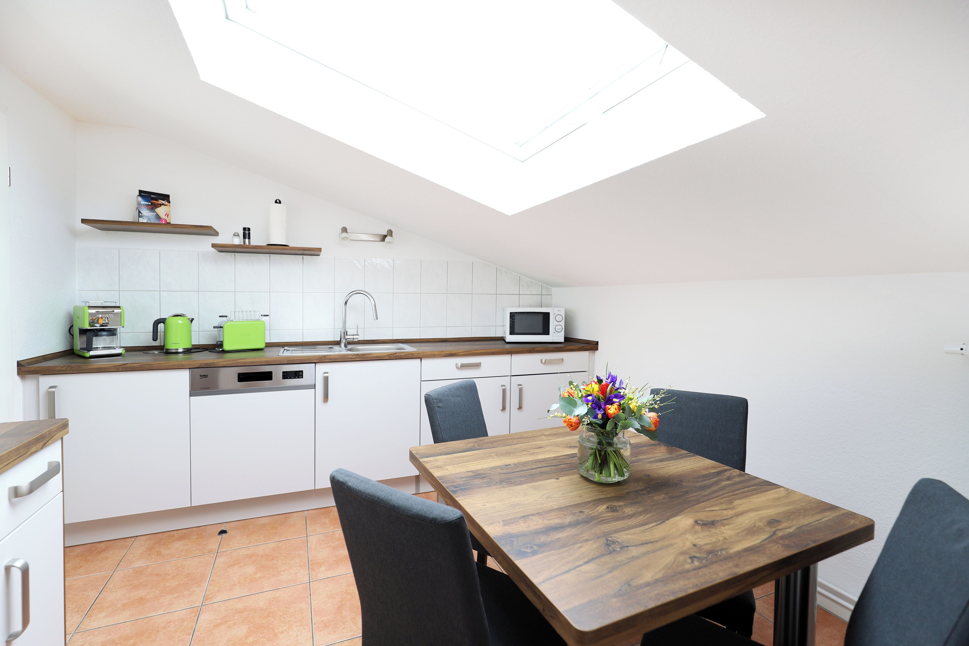 A kitchen with white cabinets, a wooden countertop, a dining table with chairs, and a skylight.