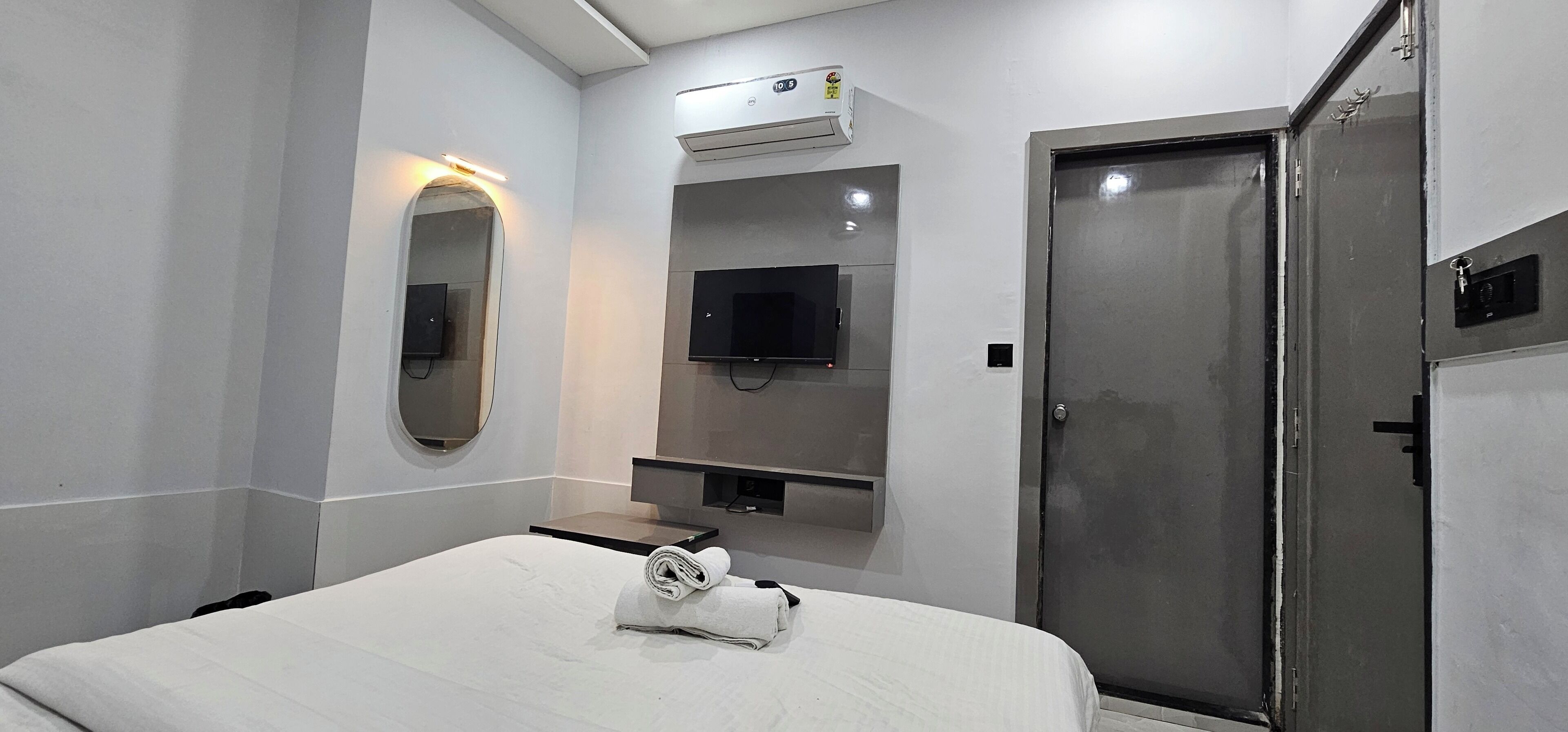 Een hotelkamer met een bed, een aan de muur bevestigde televisie, een spiegel en een deur.