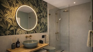 A modern bathroom with a round mirror, a vessel sink, a toilet, and a glass-enclosed shower. - LAKE Loft Living - Pflummernhaus (Überlingen)
