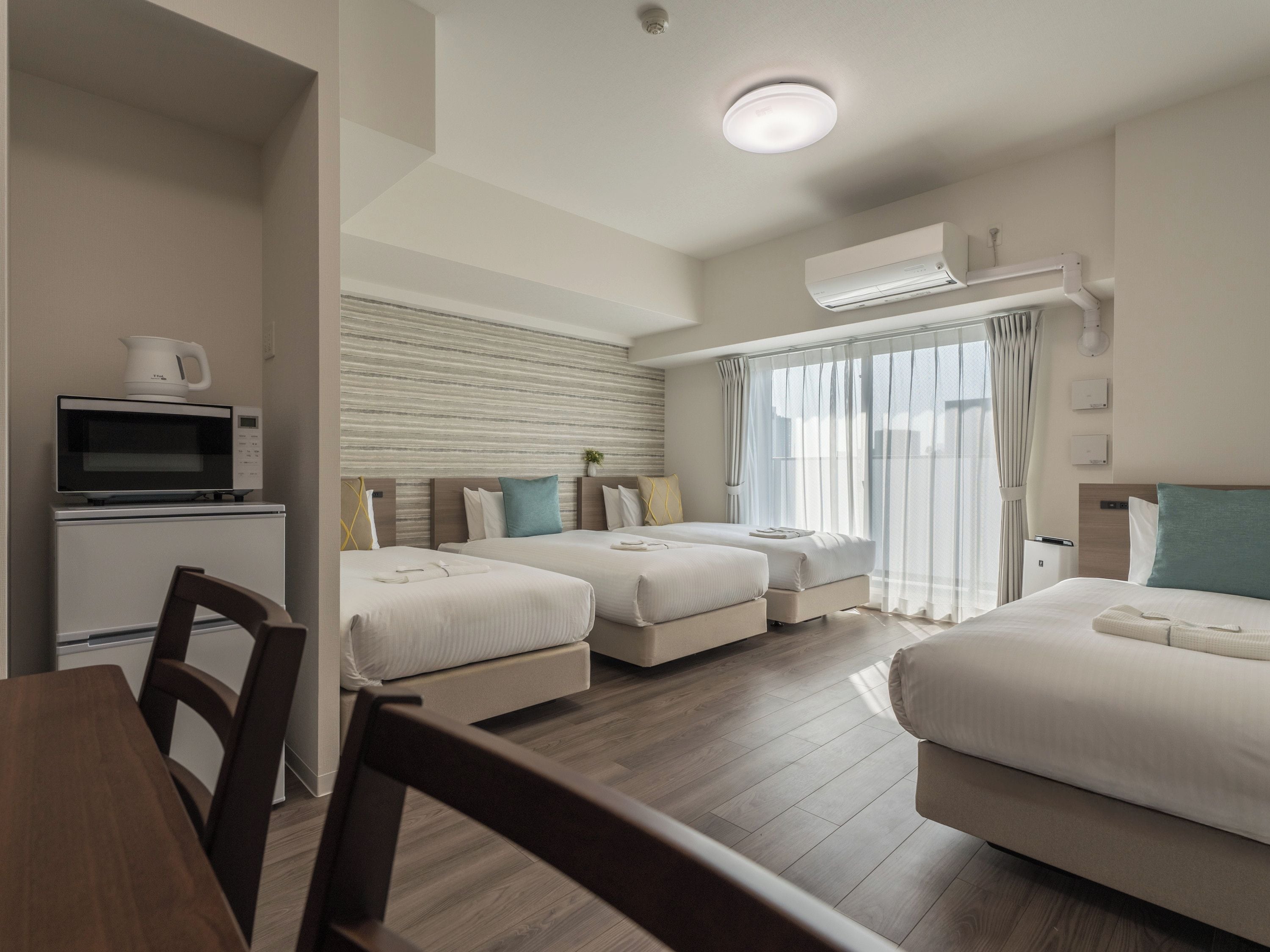 Een hotelkamer met twee bedden, een eettafel, een magnetron en een airconditioner.