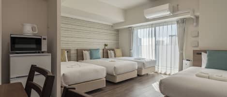 A hotel room with two beds, a dining table, a microwave, and an air conditioning unit.