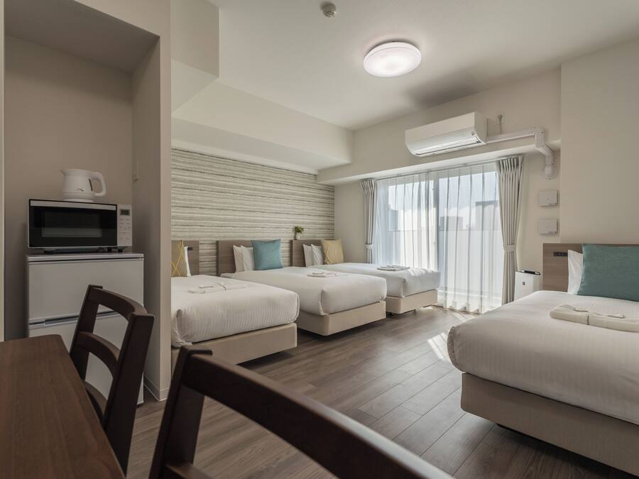 A hotel room with two beds, a dining table, a microwave, and an air conditioning unit.