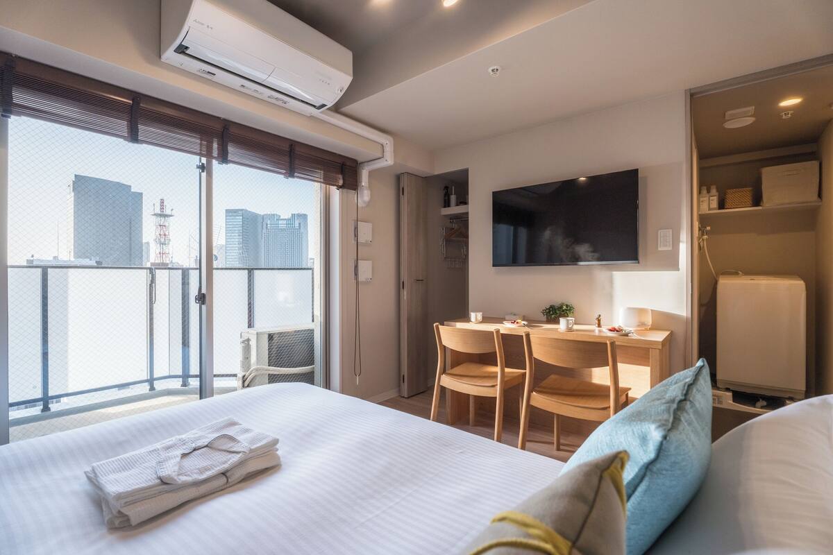 A hotel room with a bed, a desk, a chair, a TV, and a balcony with a city view.