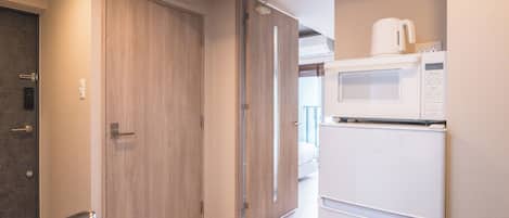 Una cocina compacta con microondas y refrigerador, una puerta de madera y un lavamanos con grifo.