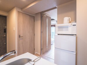 A compact kitchen with a microwave and refrigerator, a wooden door, and a sink with a faucet. - ESLEAD HOTEL Namba East (Osaka)
