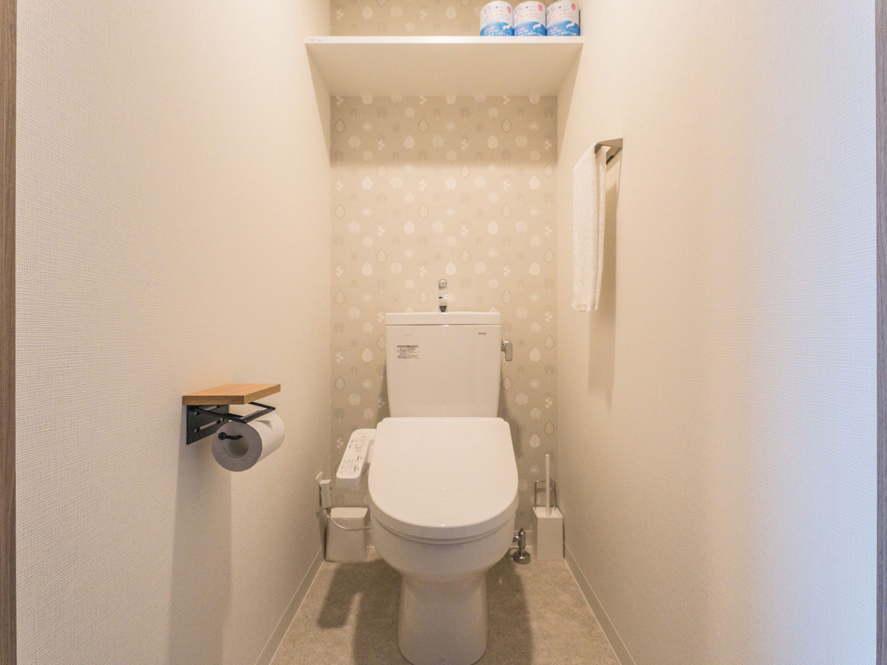 Une petite salle de bain compacte, équipée de toilettes, d’un porte-rouleau de papier toilette et d’une étagère au-dessus des toilettes.