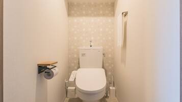 Une petite salle de bain compacte, équipée de toilettes, d’un porte-rouleau de papier toilette et d’une étagère au-dessus des toilettes.