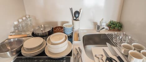 A kitchen counter with various utensils, plates, bowls, and a sink.