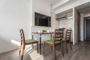 Eine moderne Küche mit Flachbildfernseher, Holzstühlen mit grünen Kissen und einem Esstisch.