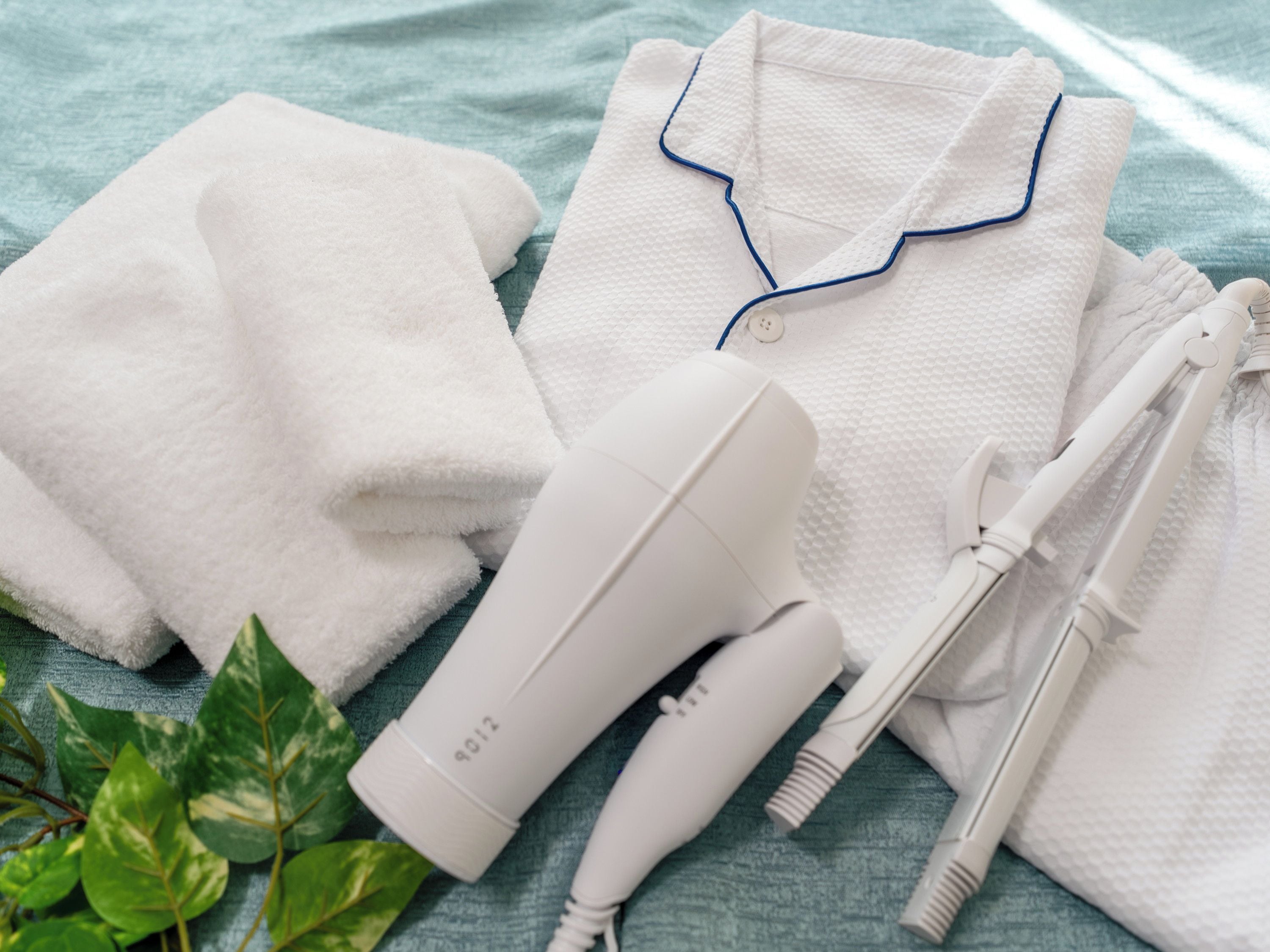 A white hairdryer, two white towels, and a white hairbrush on a blue textured surface.