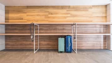 Een kamer met een houten wand, een metalen schapkas en twee koffers op de vloer.