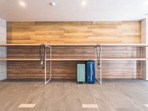 A room with a wooden wall, a metal shelf unit, and two suitcases on the floor. - ESLEAD HOTEL Namba East (Osaka)