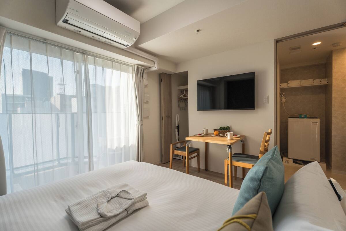 A hotel room with a bed, a desk, a TV, and a shower area.