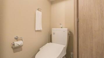 A small, compact bathroom with a white toilet, a towel hanging on a metal hook, and a roll of toilet paper on a holder.