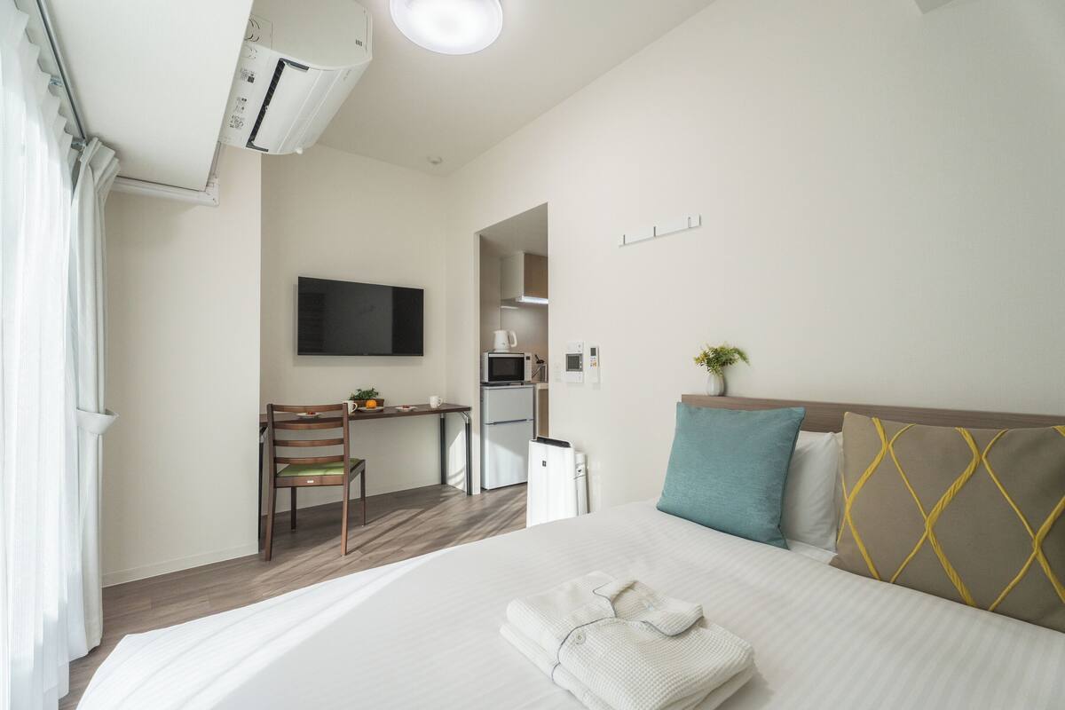 A hotel room with a bed, a desk, a television, a kitchenette, and a bathroom.